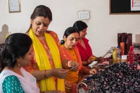 Indian mid adult female manager guiding workers cutting printed fabrics on table in textile factory and representing women empowerment